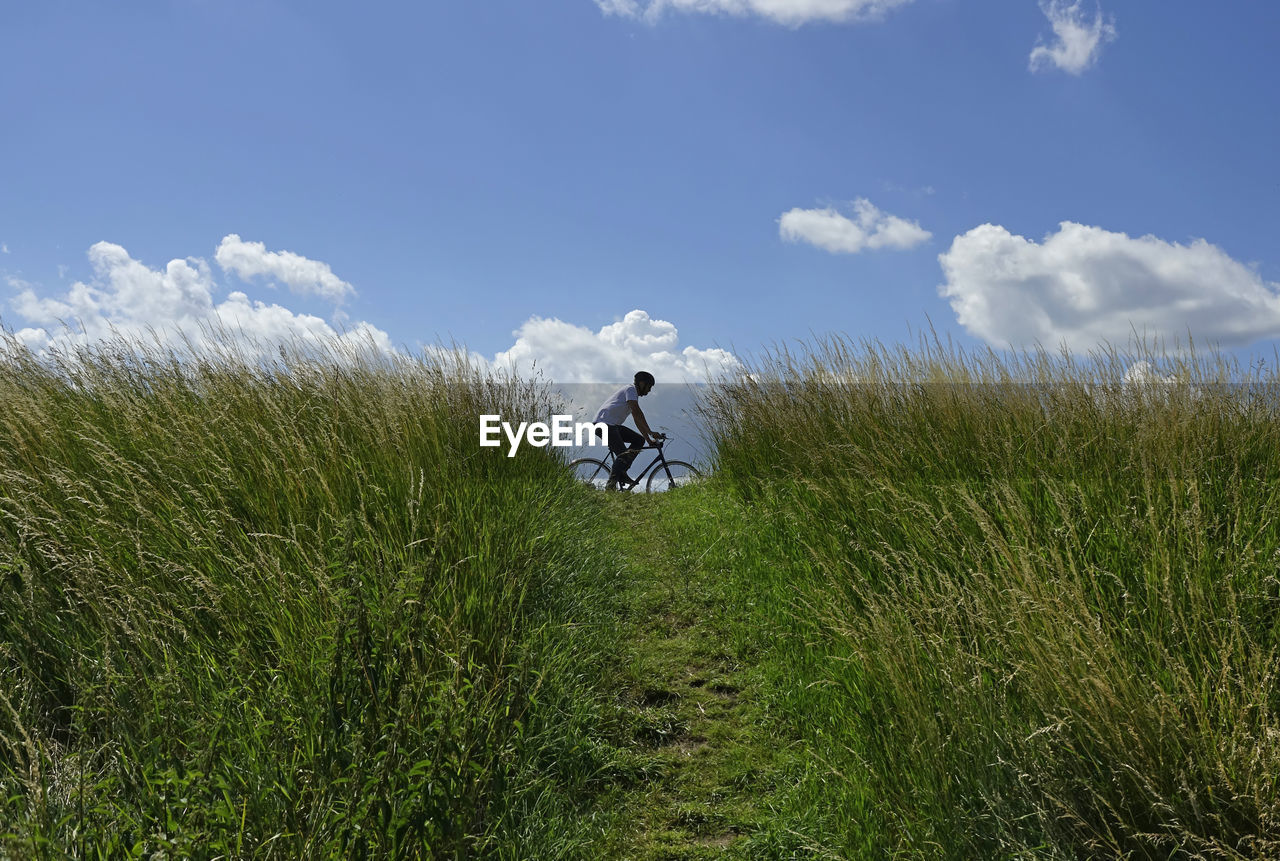 Man cycling on field  against sky