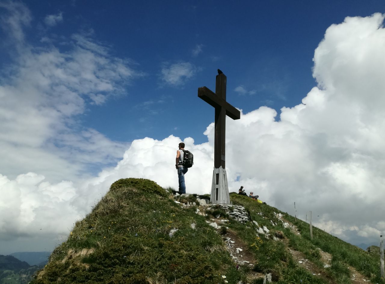 Man standing on mountain by cross against sky