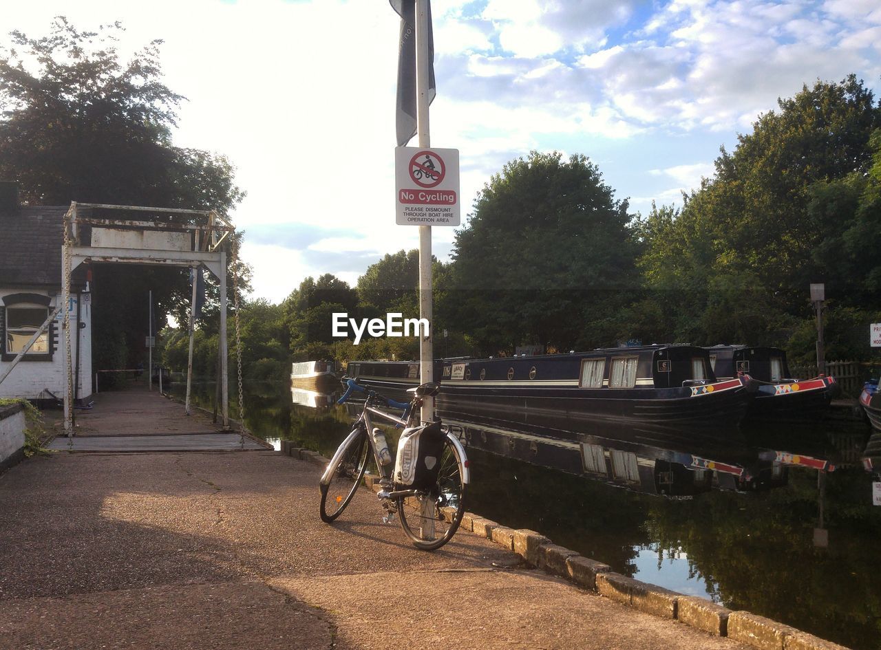 BICYCLE PARKED BY TREE AGAINST SKY