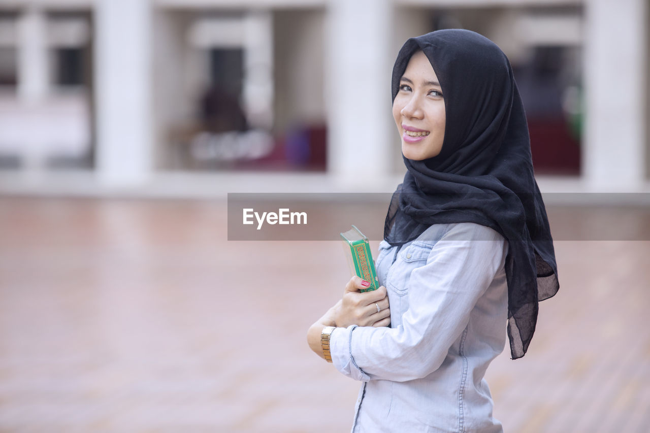 Portrait of woman holding kuran while standing in mosque