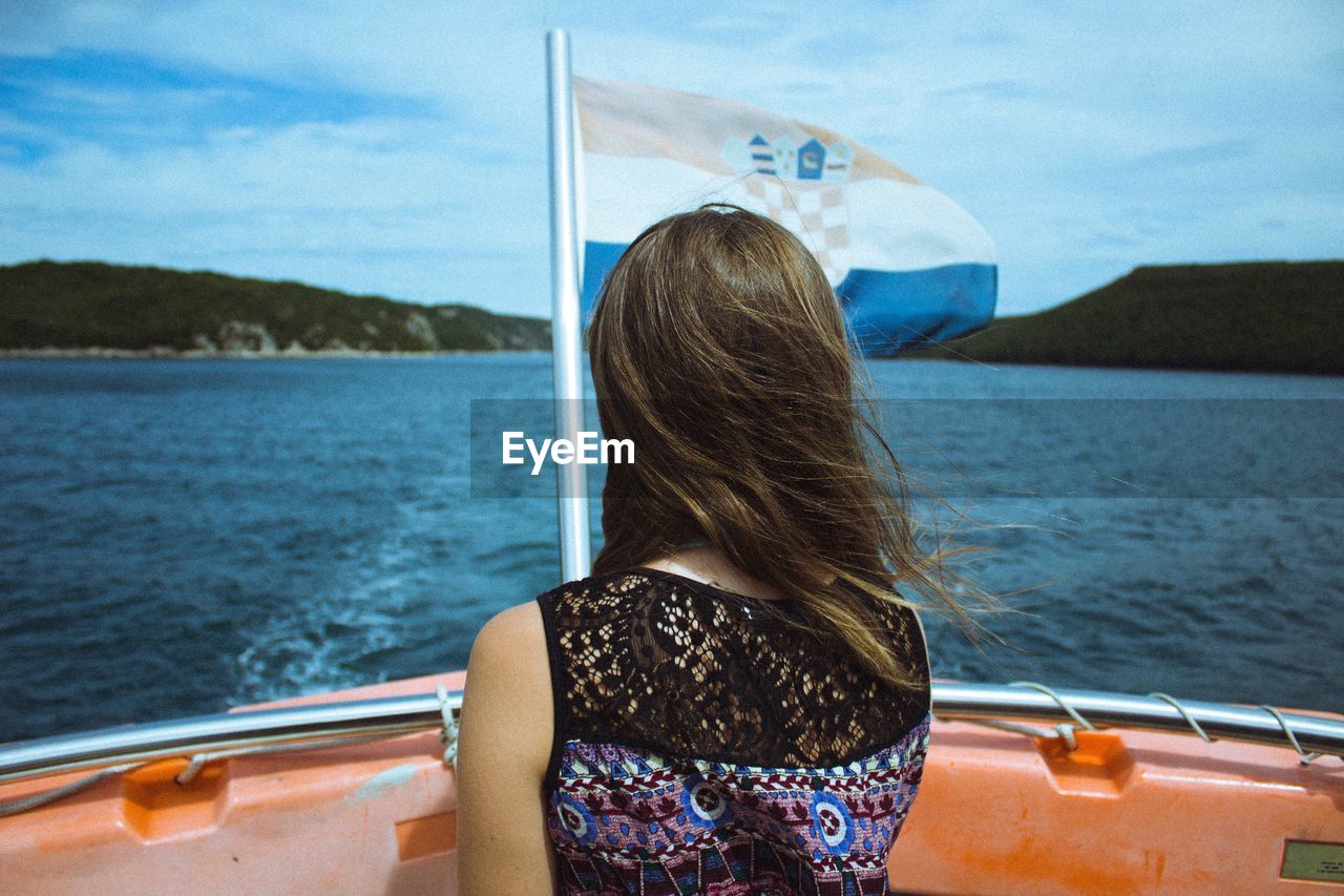 Rear view of woman by croatian flag in boat on lake