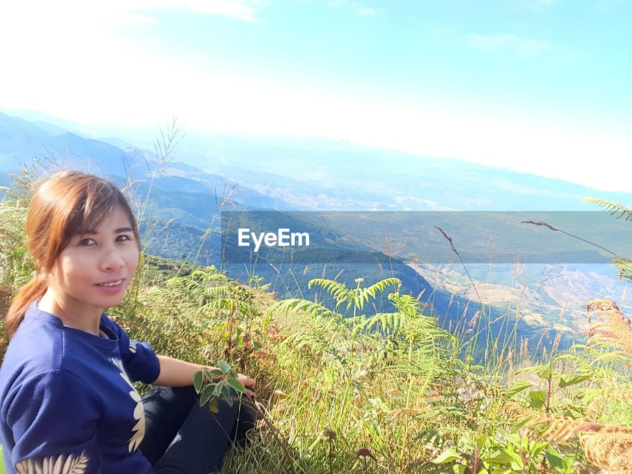 PORTRAIT OF SMILING YOUNG WOMAN AGAINST MOUNTAIN RANGE