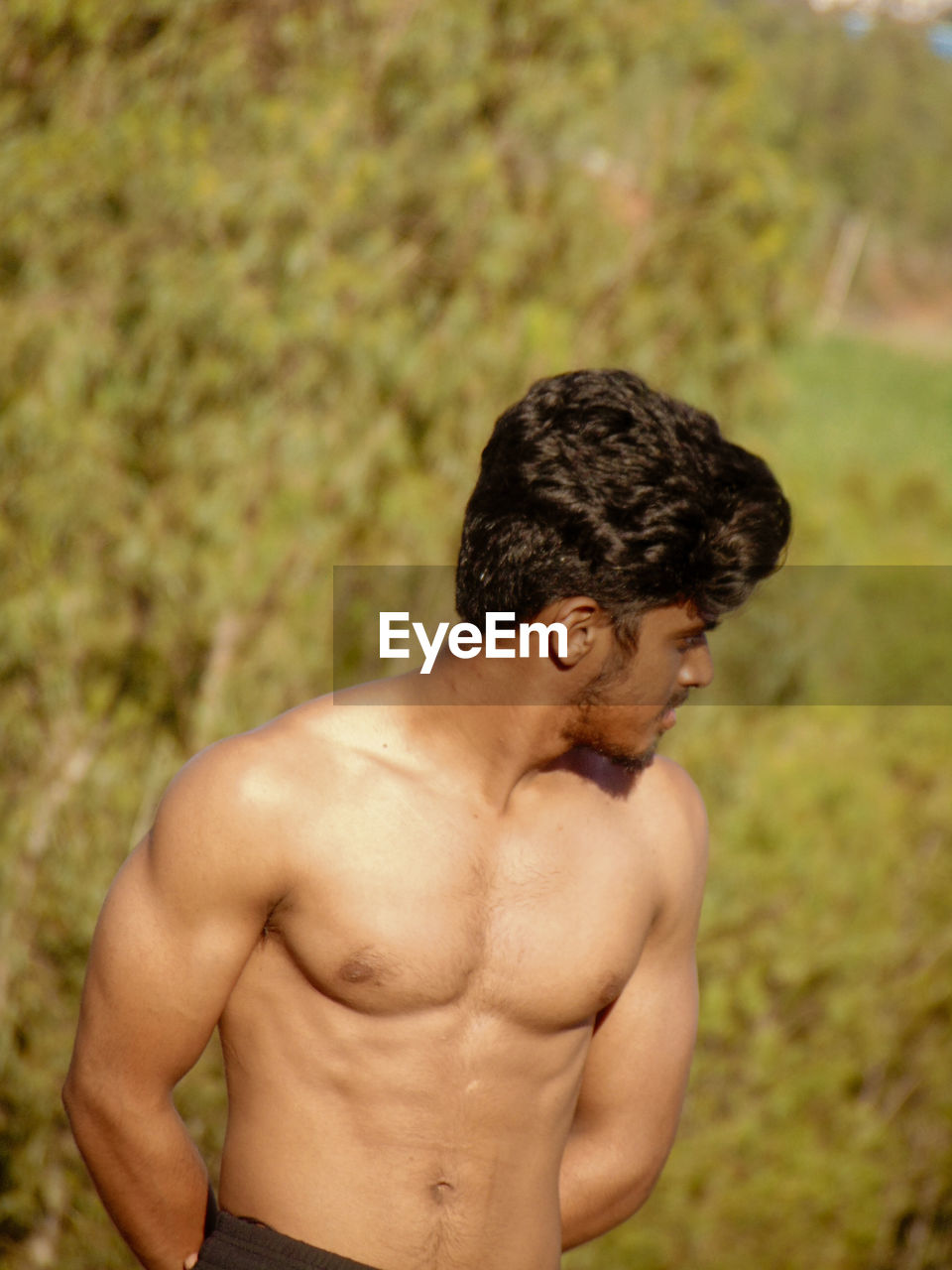 Shirtless young man looking away while standing on land