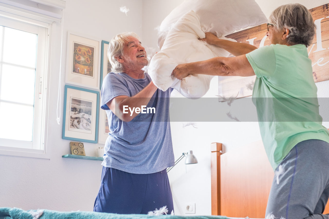 Low angle view of senior couple pillow fighting at home