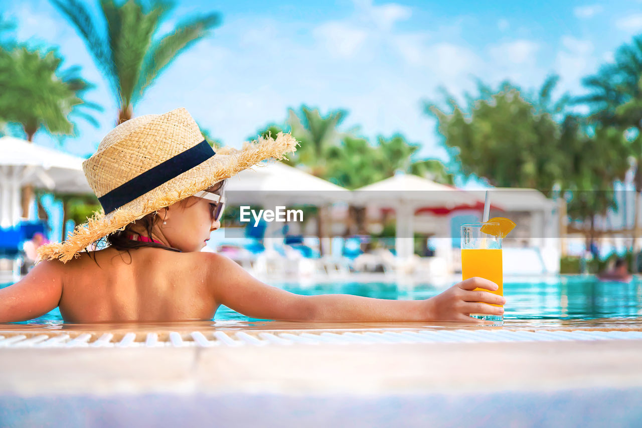 Rear view of girl holding juice glass at poolside