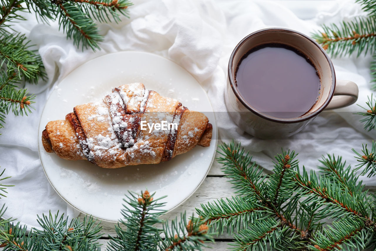 Christmas breakfast. cup of coffee, croissant and tree fir branches on window sill