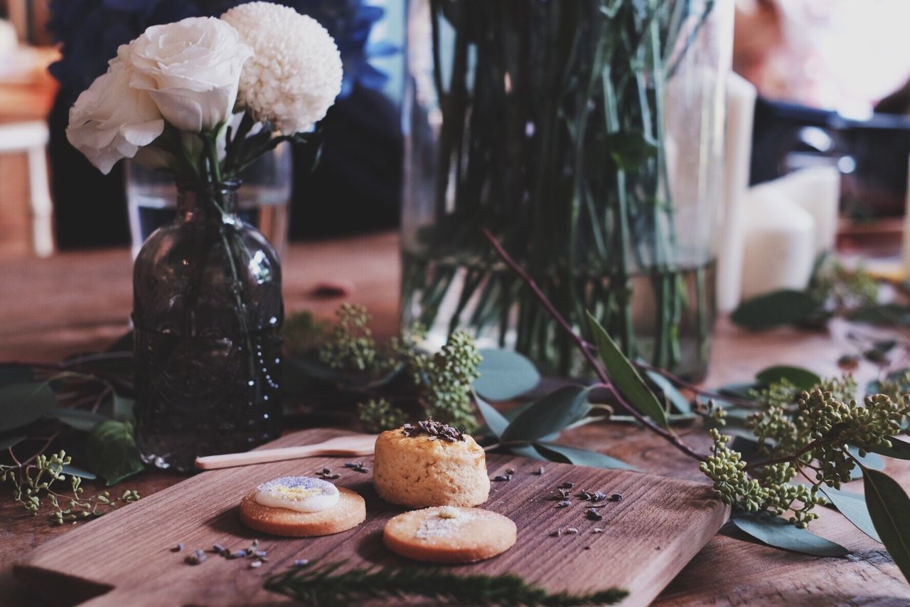 Close-up of cookies on cutting board by flowers vase on table