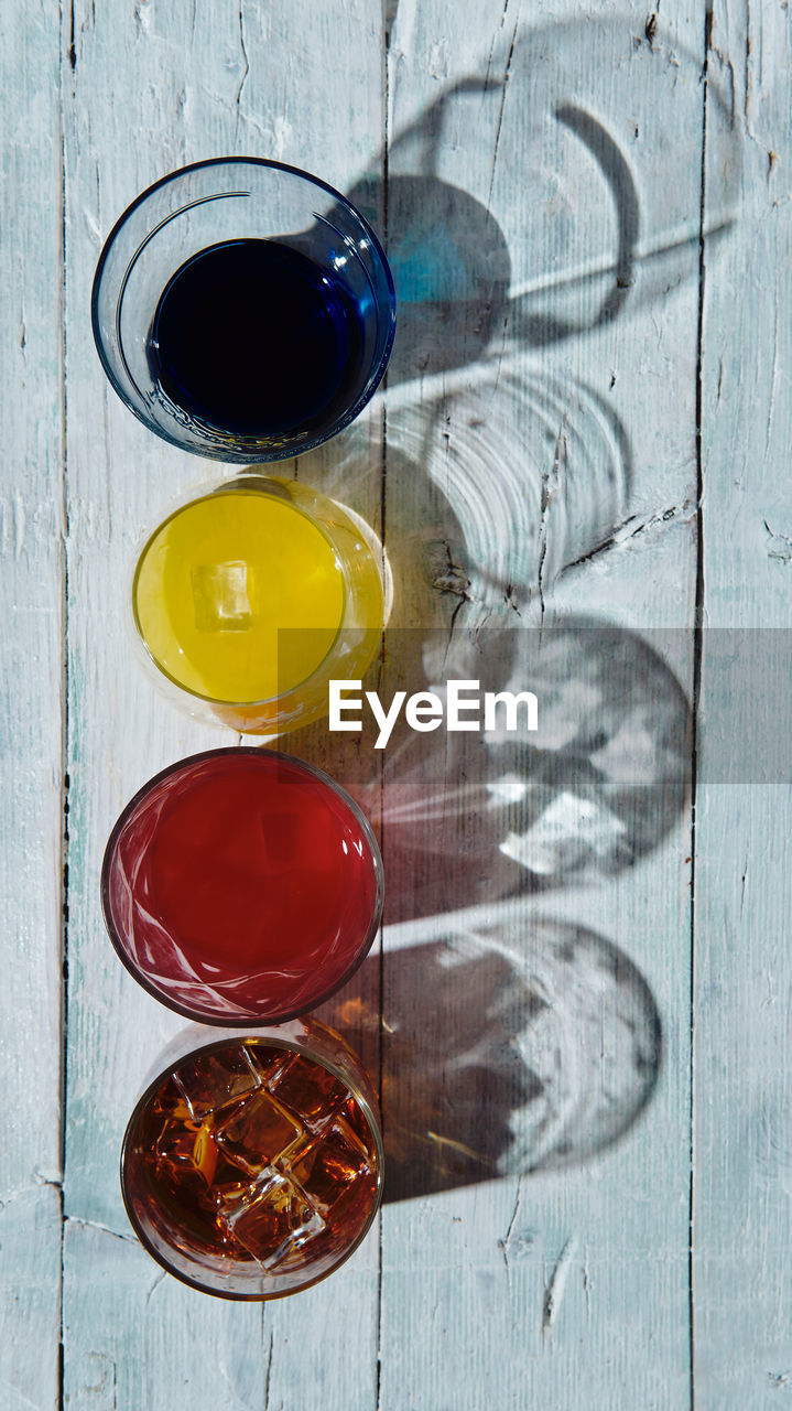 Different coloured drinks in a glass on a white wooden base