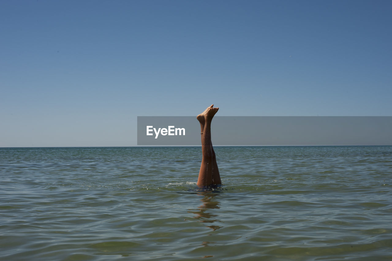 Woman swimming with feet up in sea against clear blue sky