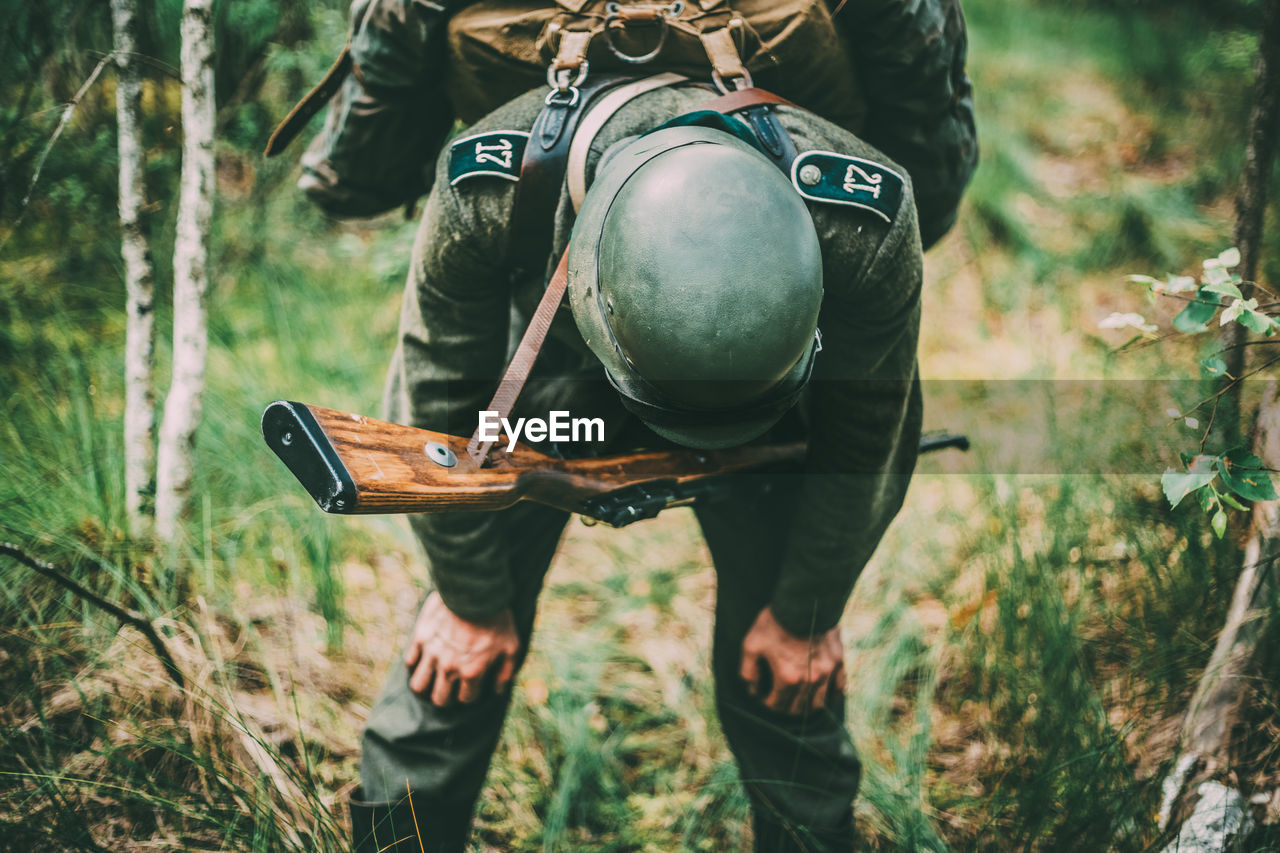 Tired soldier with rifle standing in forest