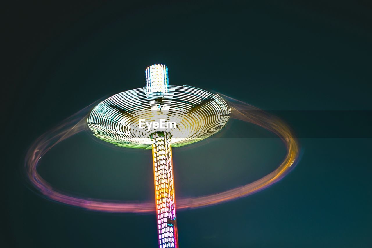 Low angle view of illuminated chain swing ride against clear sky at night