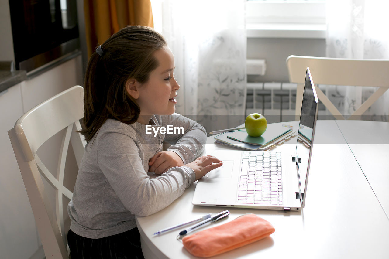 Side view of girl studying over laptop at home