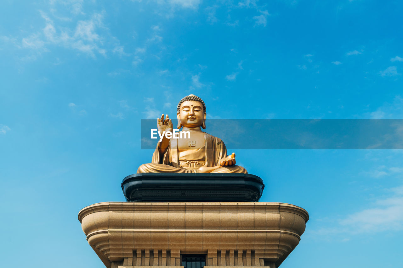 Low angle view of buddha statue against blue sky