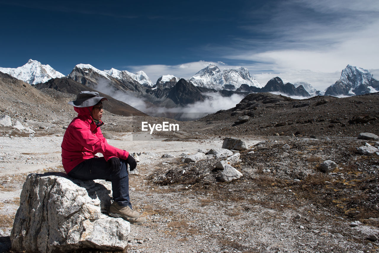 Side view of mid adult woman sitting on rock against sky during sunny day