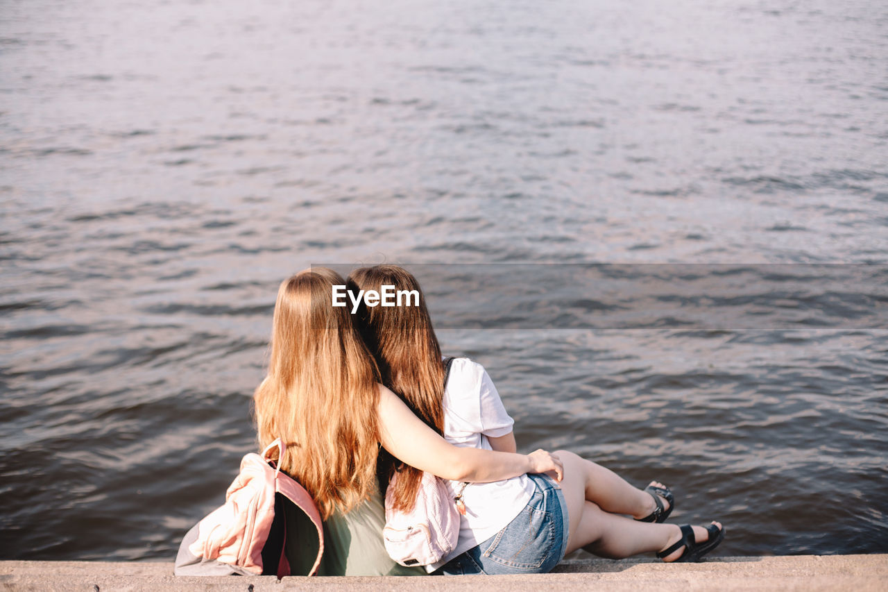 Back view of lesbian couple embracing while sitting on steps by river