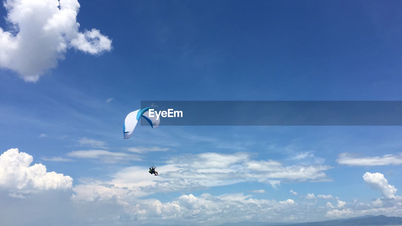 Low angle view of paragliding against blue sky