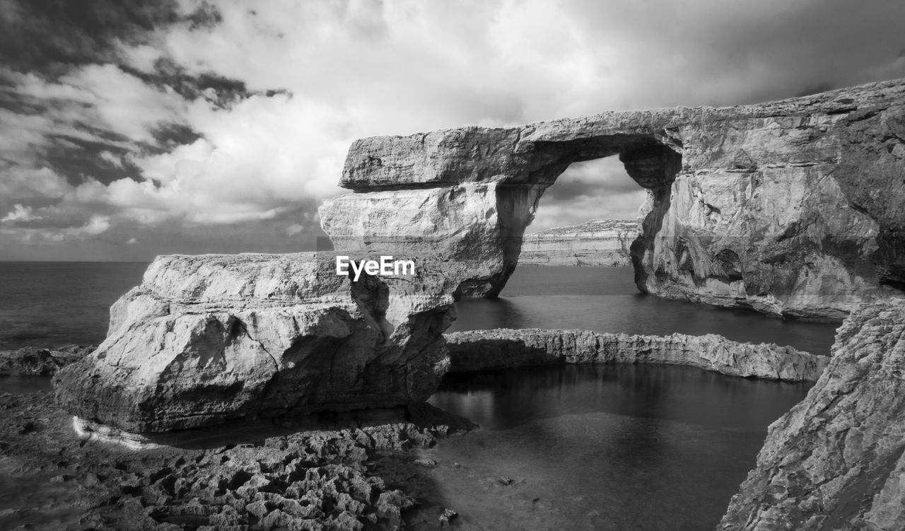 Lake and rock formation against cloudy sky