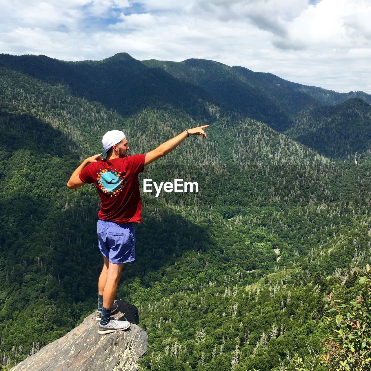 Rear view of male hiker standing on rock against landscape