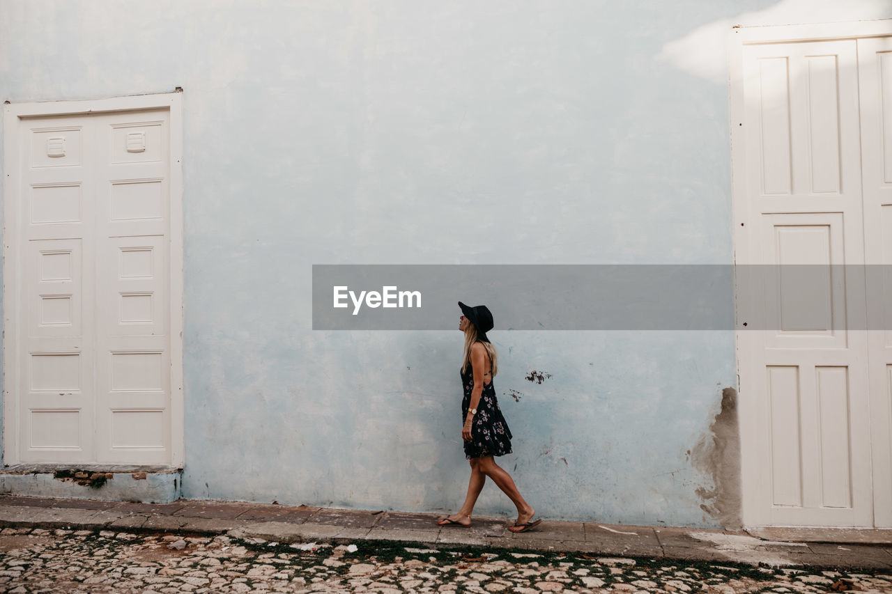 Woman in hat walking against house