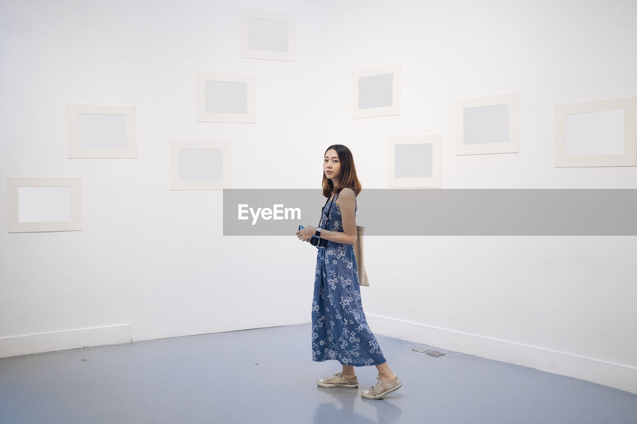 YOUNG WOMAN STANDING AGAINST WALL AT HOME