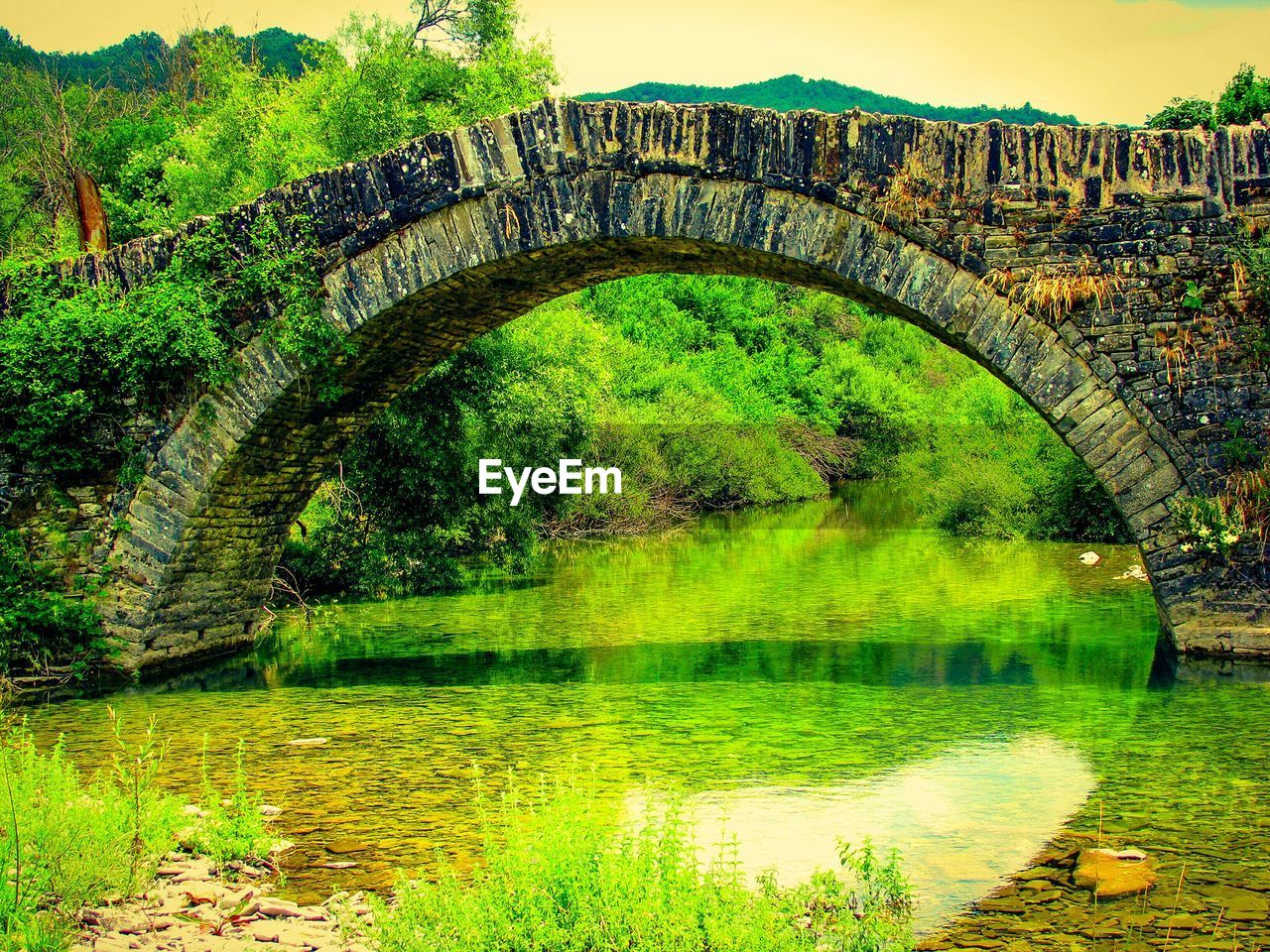 BRIDGE OVER RIVER WITH TREES IN BACKGROUND