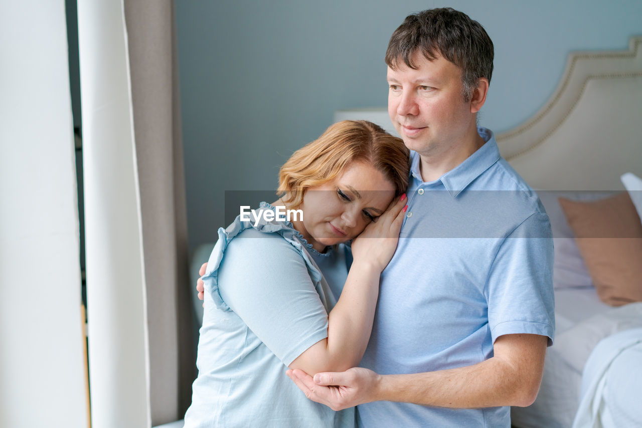 Dreamy couple family connection cuddling looking into distance through window.