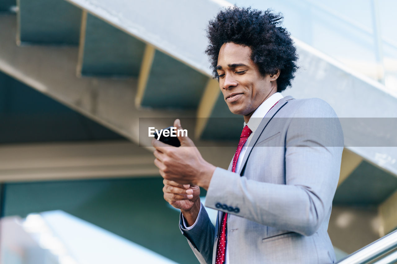 Smiling businessman holding smart phone outdoors