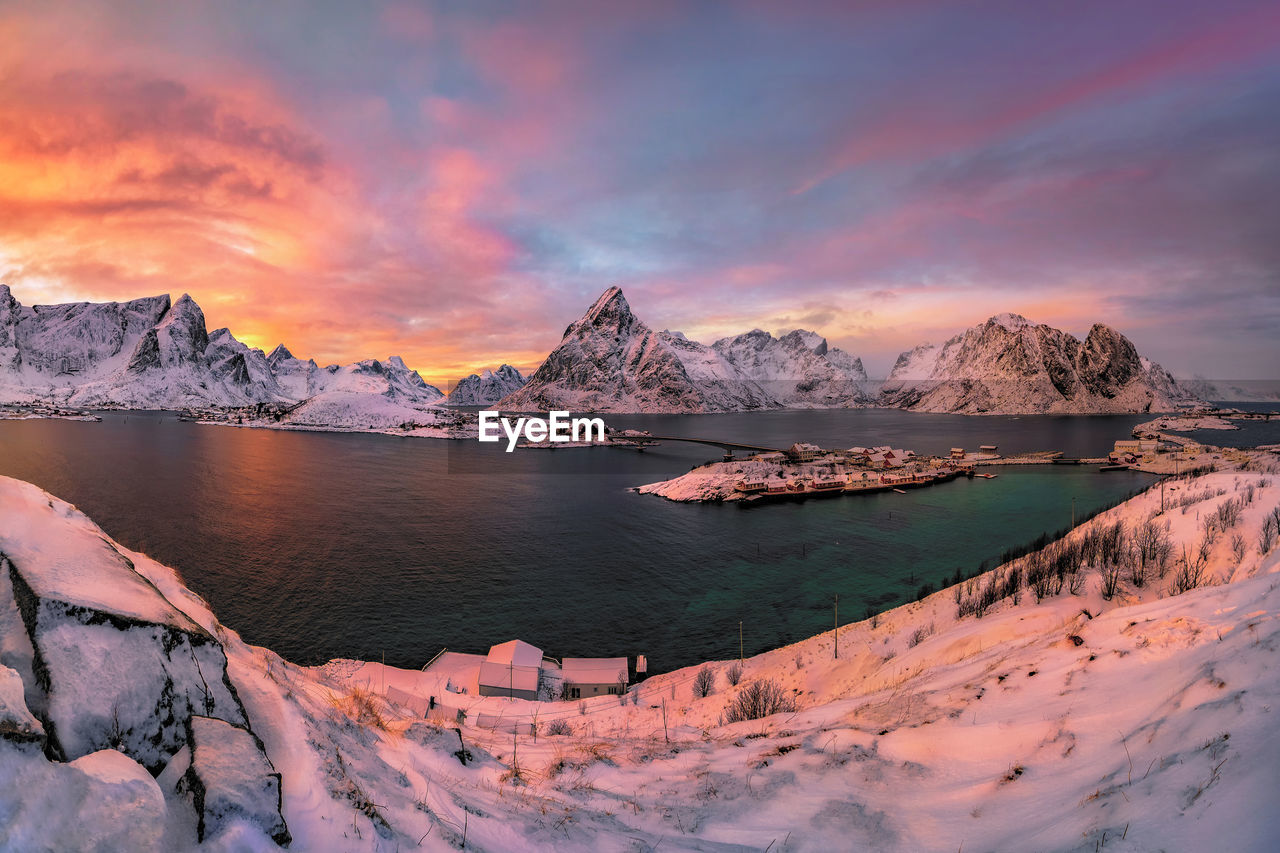 Scenic view of lake by snowcapped mountains against sky during sunset