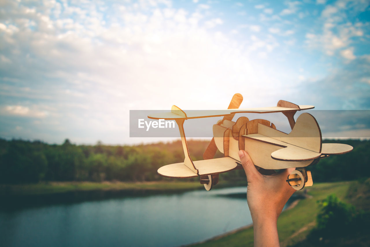 Cropped hand holding model airplane by lake