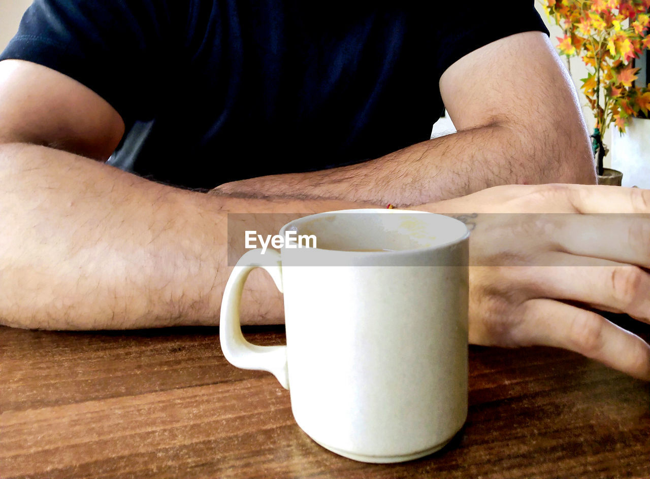 MIDSECTION OF MAN HOLDING COFFEE CUP AND TABLE