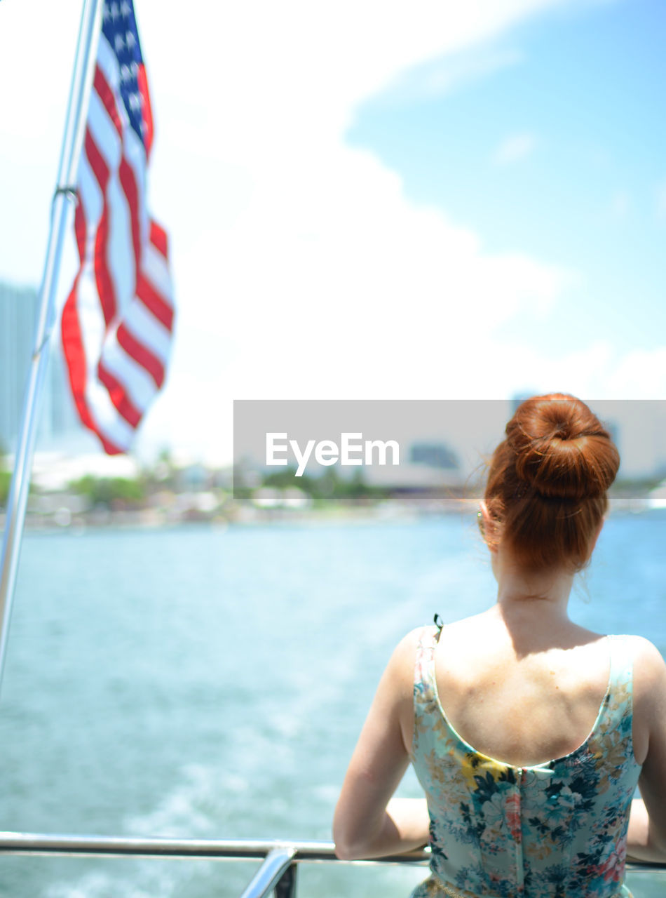 Rear view of woman looking at sea while traveling on boat with flag