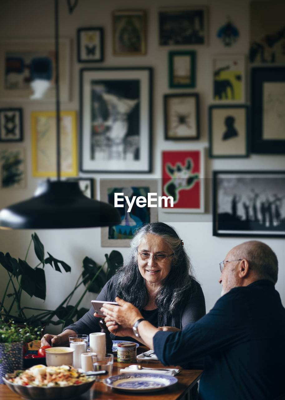 Senior man showing mobile phone to woman at dining table