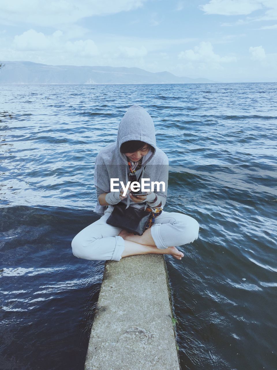 Woman using mobile phone while sitting on rock in river