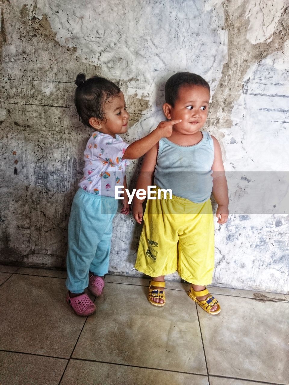  sister touching cheek of brother while standing against wall