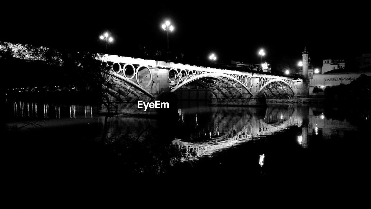 BRIDGE OVER RIVER AGAINST ILLUMINATED AT NIGHT