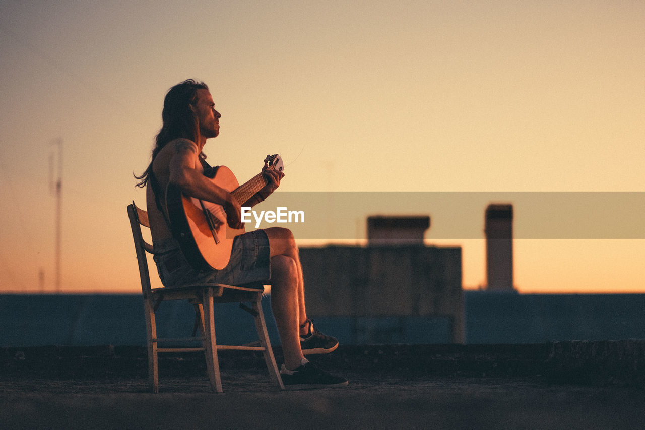 Young man playing accousting guitar on rooftop