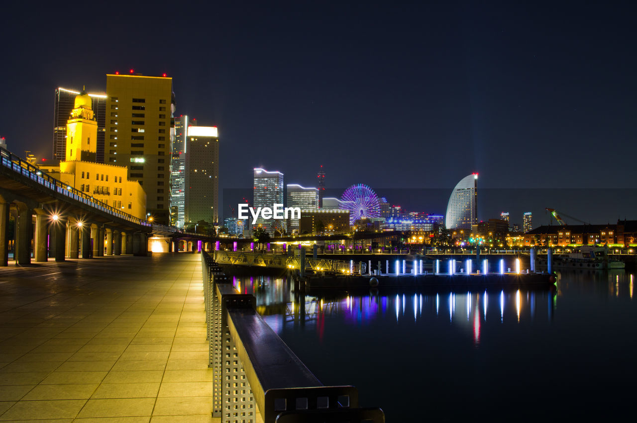 Illuminated buildings by river against sky at night