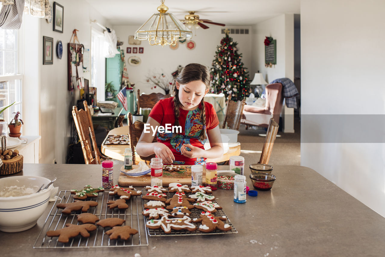 Girl sitting at kitchen counter decorating christmas cookies