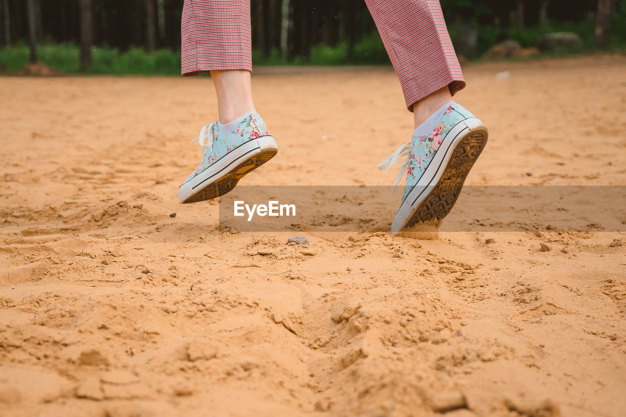 The legs of a girl in sneakers run along a sandy beach. sports recreation on the coast