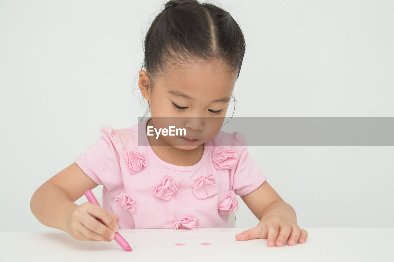 Cute girl drawing on paper against wall at home