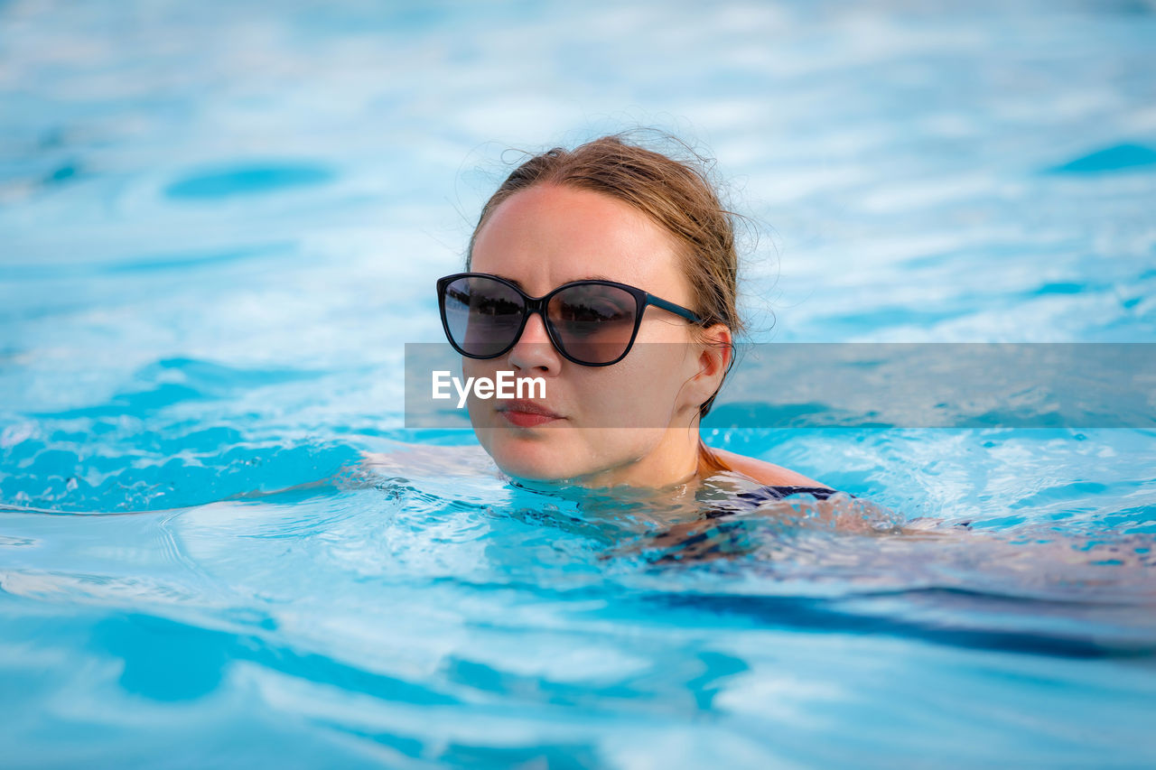 A young, beautiful girl in sunglasses swims in the pool. high quality photo