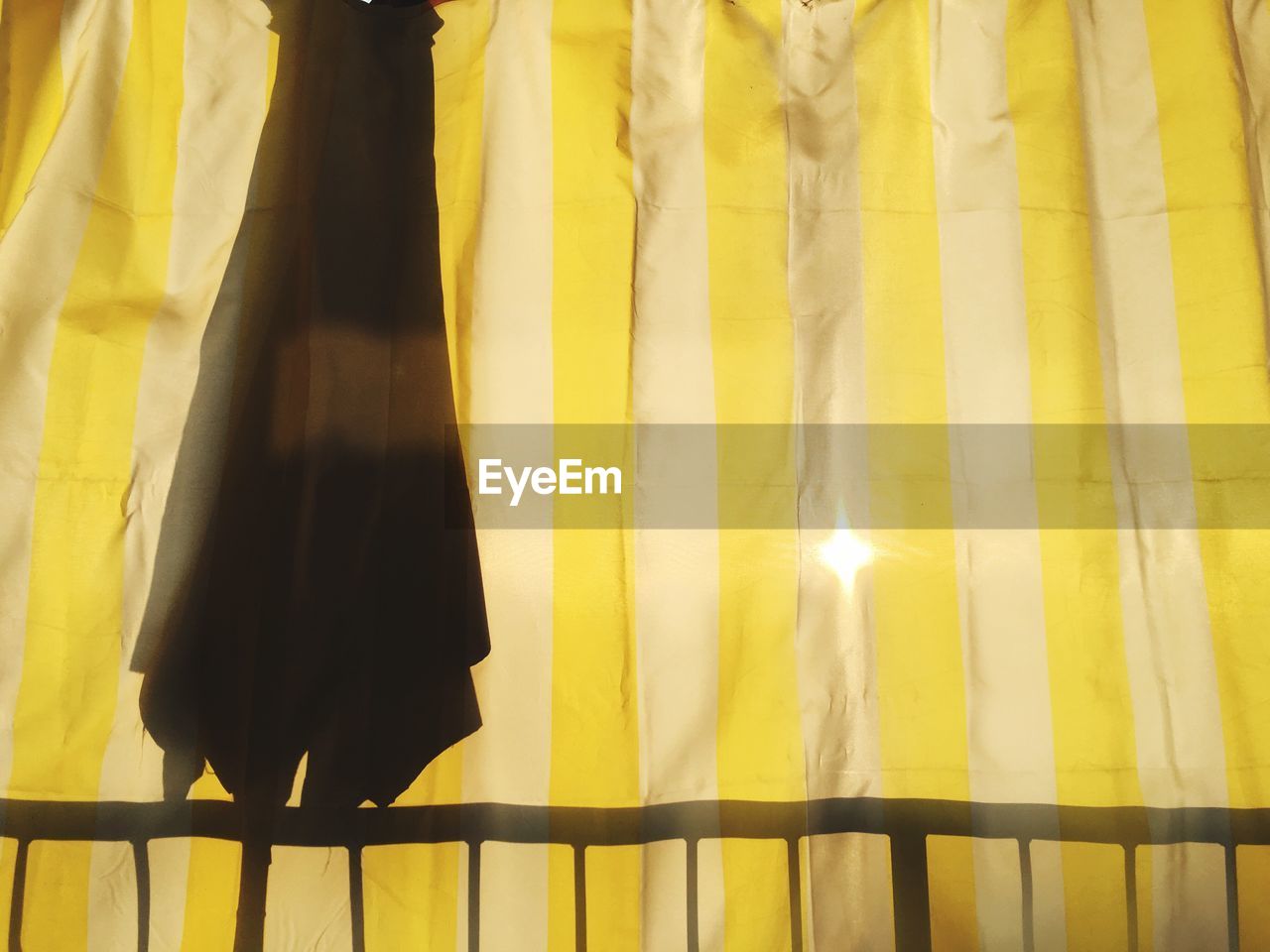 Close-up of yellow curtain with sunlight peaking through and the silhouette of a closed umbrella