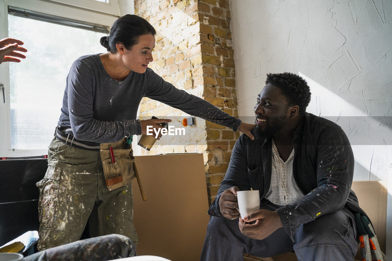 Multiracial male and female carpenters talking during coffee break in apartment