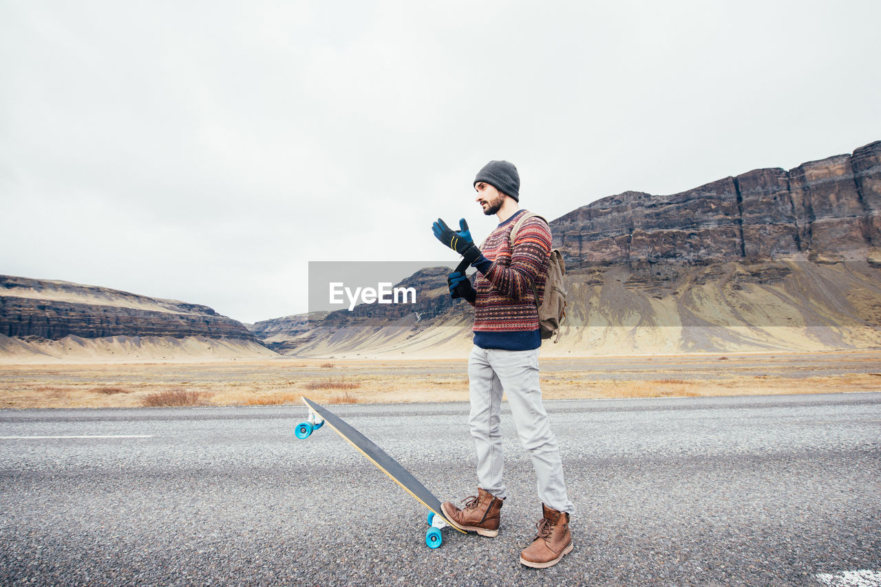 Full length of man standing with skateboard on road against sky