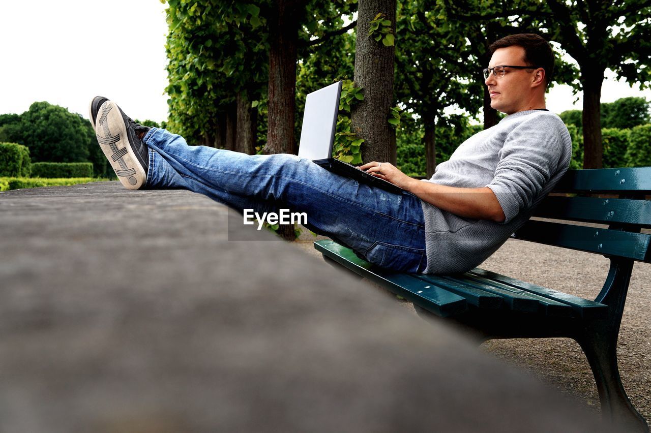 Man using laptop while sitting on bench in park