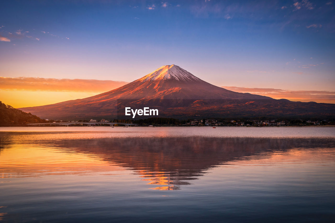 Scenic view of lake by mountain against sky during sunset