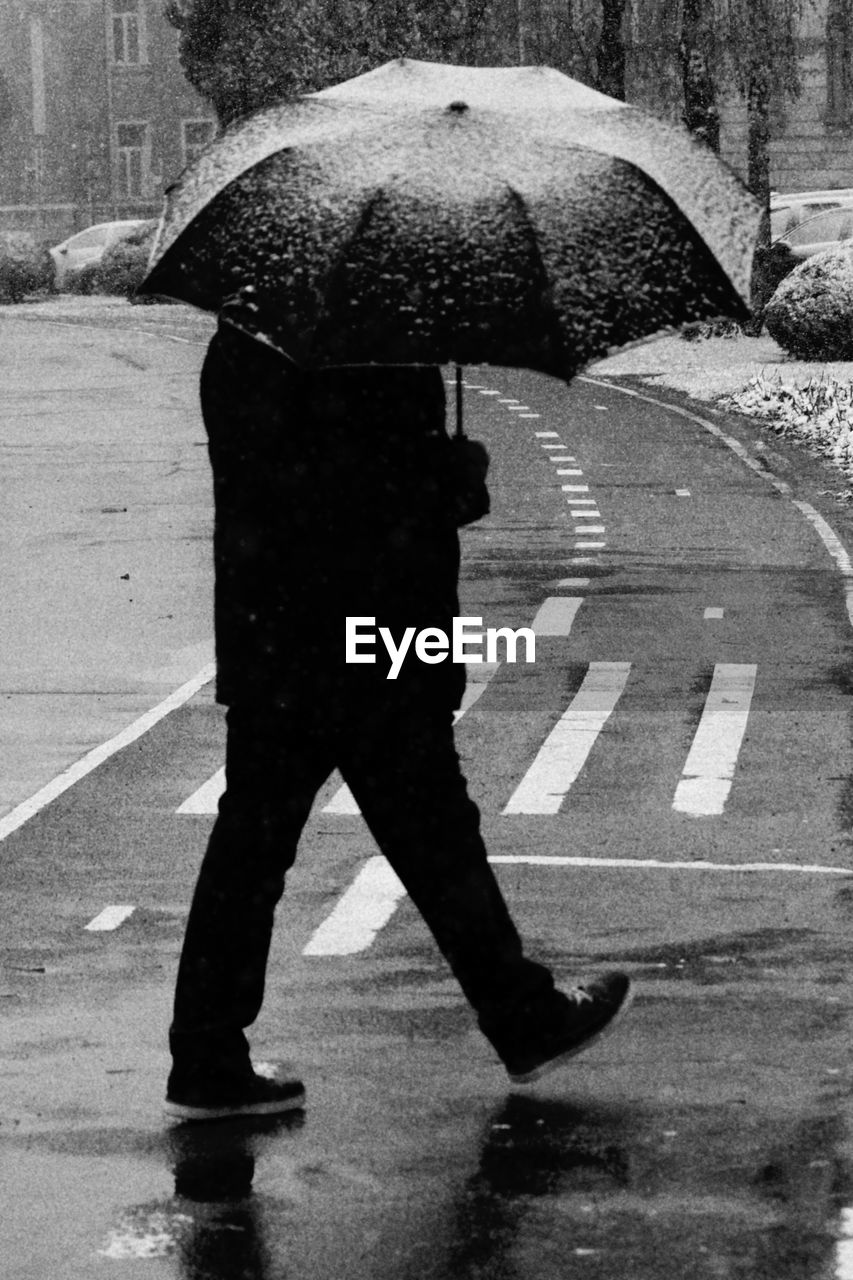 Man holding umbrella while walking on road