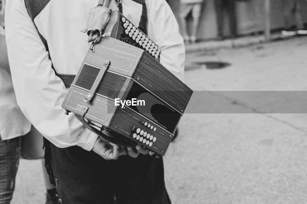Midsection of man carrying accordion while standing on road