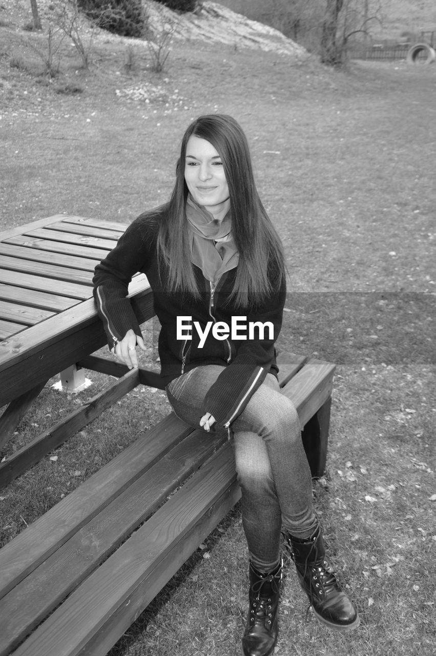 PORTRAIT OF WOMAN SITTING ON BENCH AT PARK