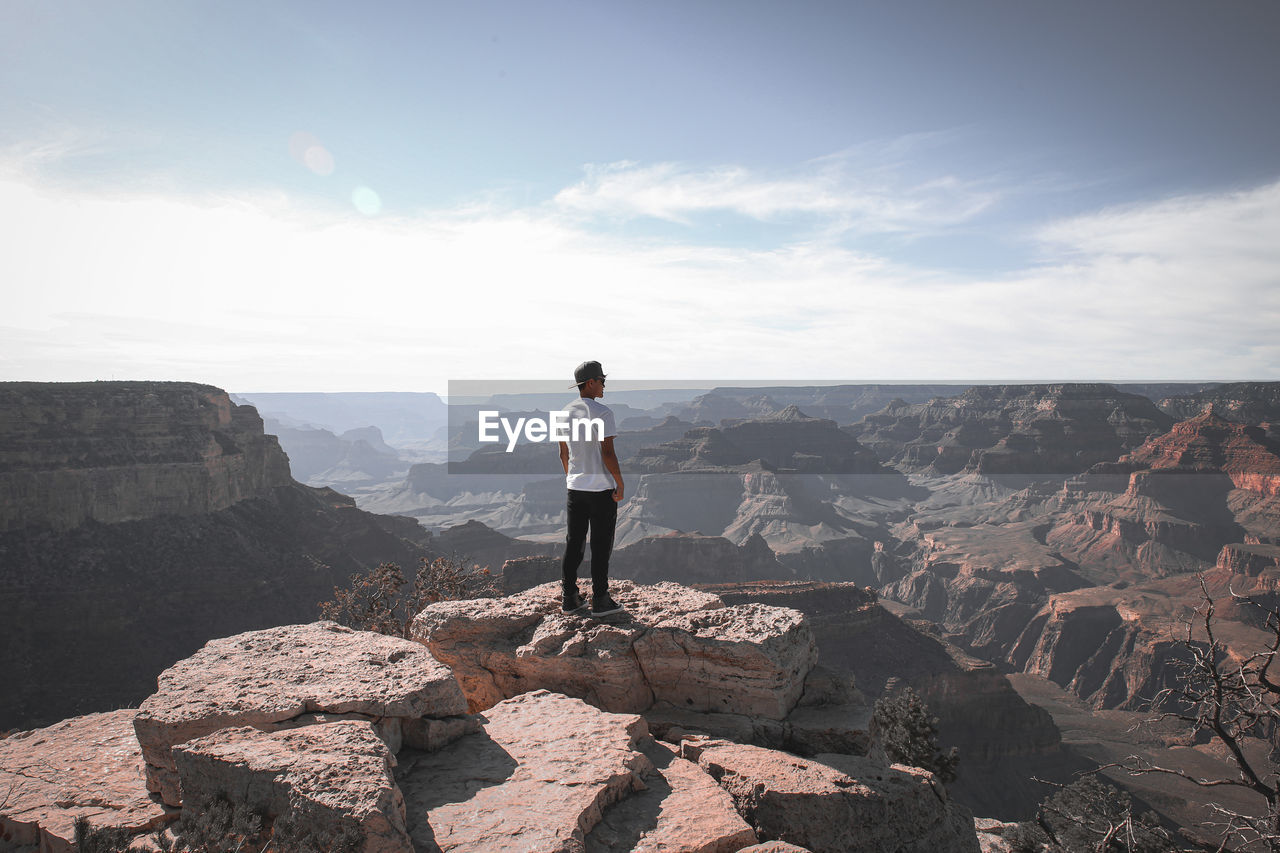 rear view of man walking on rock against sky